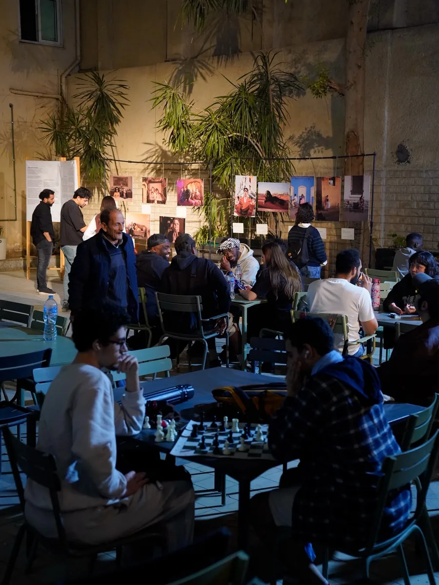 Des participants jouent aux échecs dans une cour, devant une exposition de photographies.