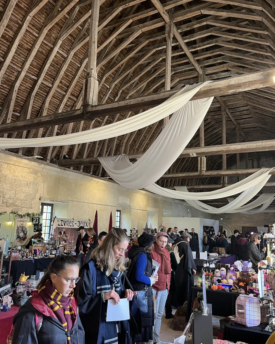 Sous la charpente d’une grange, des visiteurs déguisés en sorciers parcourent un marché de créateurs.